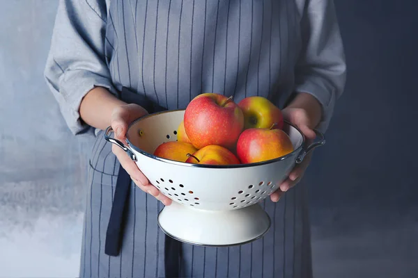 Kvinna i förkläde holding durkslag med äpplen — Stockfoto