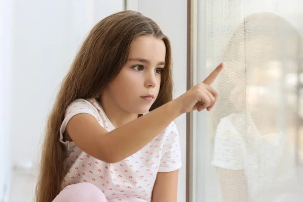 Triste petite fille dessin sur vitre à la maison — Photo