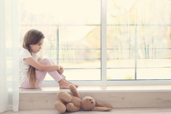 Little sad girl sitting on windowsill — Stock Photo, Image