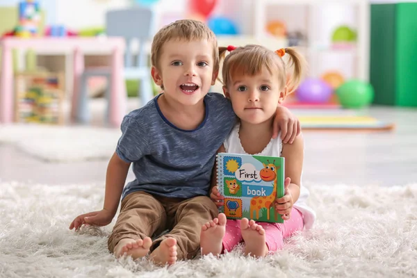 Lindos niños divertidos sentados en la alfombra con libro —  Fotos de Stock