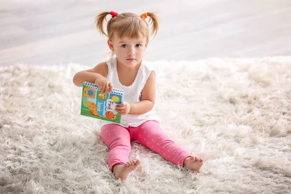 Söt liten flicka sitter på mattan med bok — Stockfoto