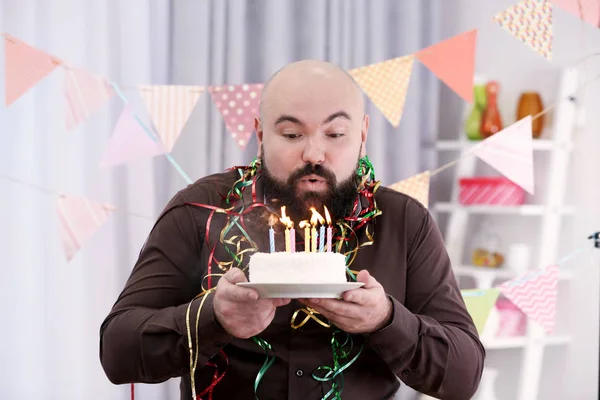 Funny fat man blowing out candles on birthday cake at party — Stock Photo, Image