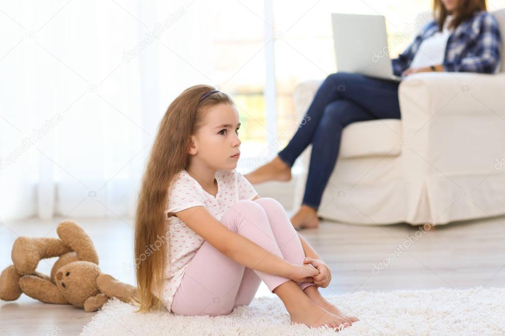 Sad little girl sitting on floor in room