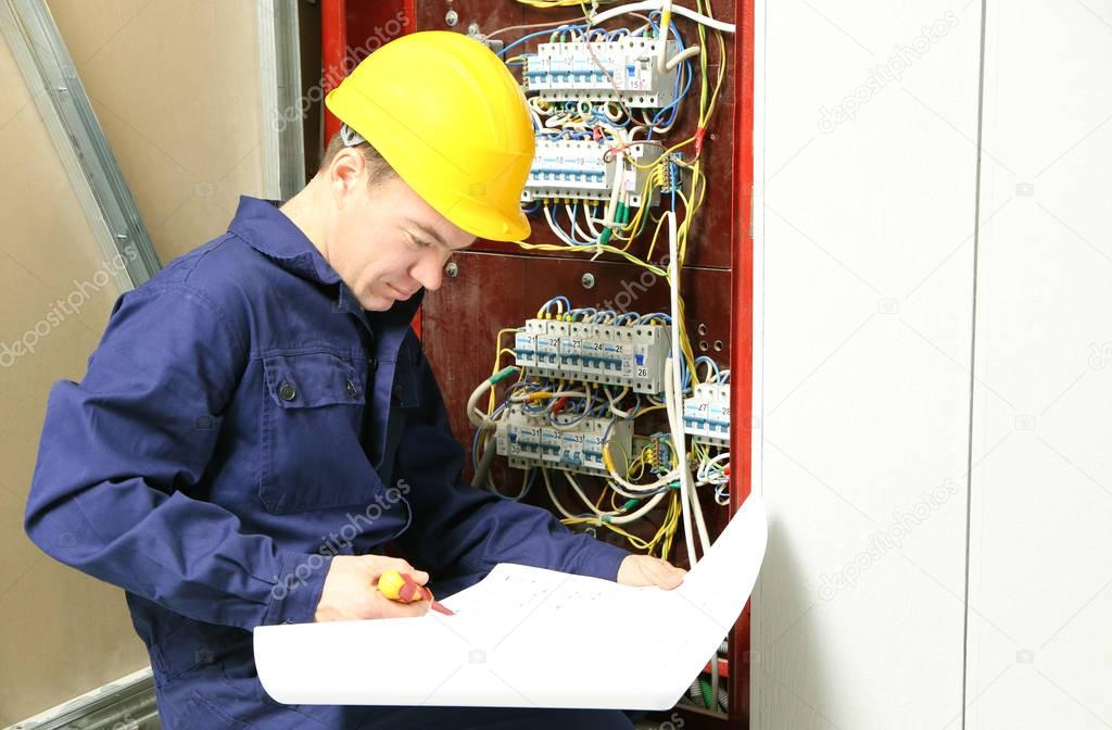 Electrician checking connections in distribution board according to wiring diagram