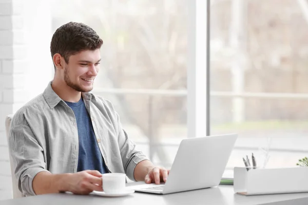 Bello giovane che lavora su laptop e beve caffè a casa — Foto Stock