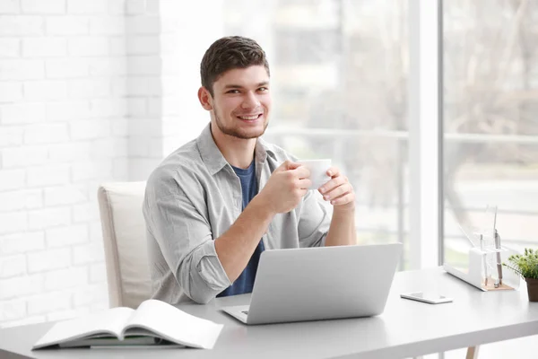 Handsome young man working on laptop and drinking coffee at home — Stock Photo, Image