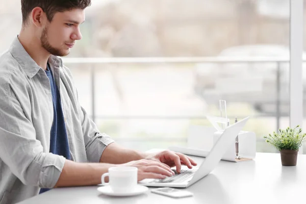 Jovem bonito trabalhando no laptop e bebendo café em casa — Fotografia de Stock