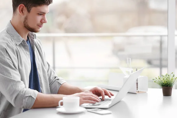 Handsome young man working on laptop and drinking coffee at home — Stock Photo, Image