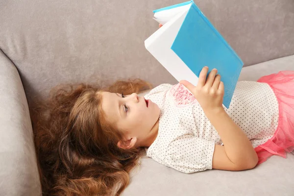 Menina pequena leitura livro no sofá — Fotografia de Stock