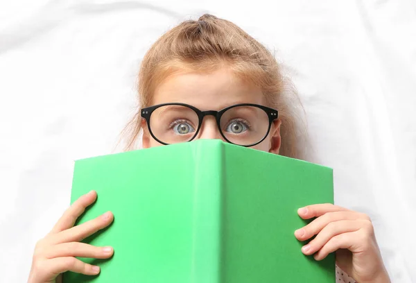 Menina bonito com livro deitado em folhas brancas — Fotografia de Stock