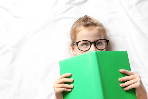 Χαριτωμένο κορίτσι με βιβλίο ξαπλωμένος σε λευκά φύλλα — Φωτογραφία Αρχείου