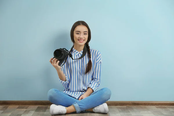 Mooie jonge fotograaf zittend op de vloer in de buurt van kleur muur — Stockfoto