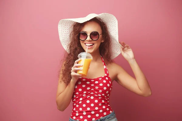 Молодая красивая женщина в шляпе с коктейлем на цветном фоне — стоковое фото
