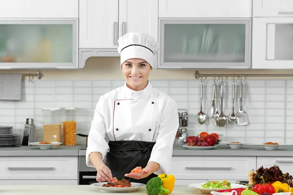 Young woman chef decorating meat dish on plate with tomato slices