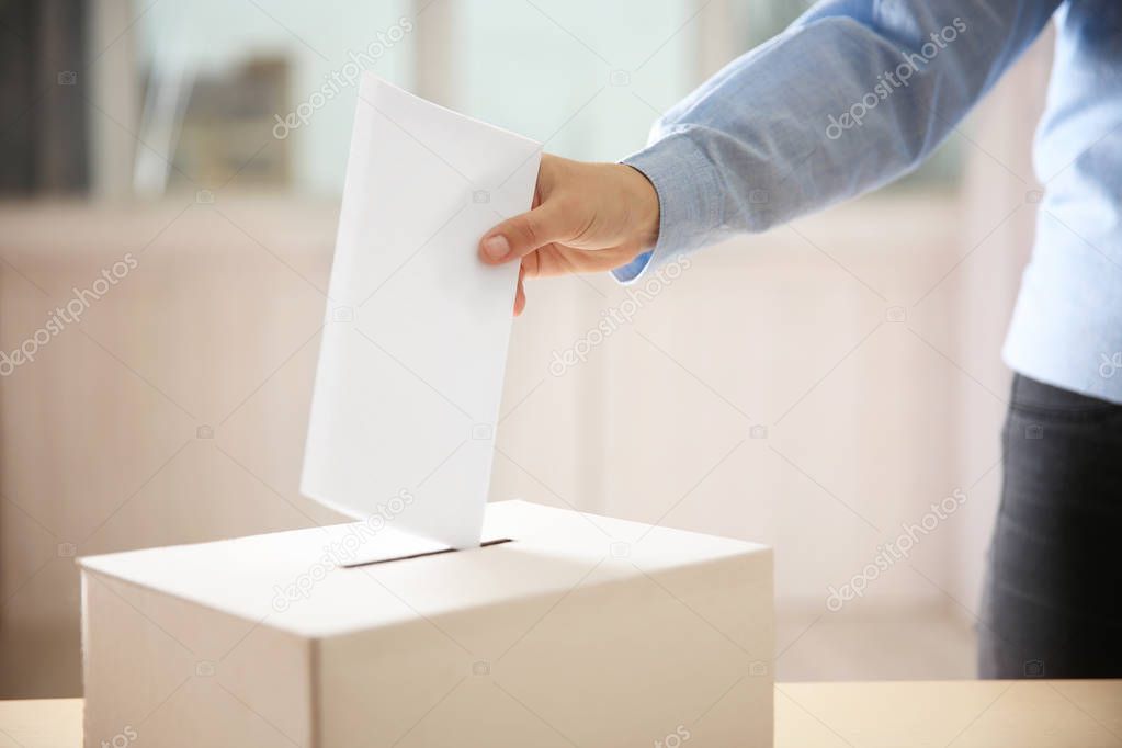 hand inserting envelope in ballot box