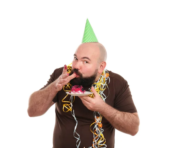 Engraçado homem gordo com chapéu de festa comendo bolo saboroso, no fundo branco — Fotografia de Stock