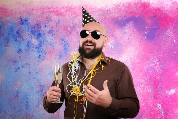 Uomo grasso divertente con cappello partito e bicchiere di champagne su sfondo di colore — Foto Stock