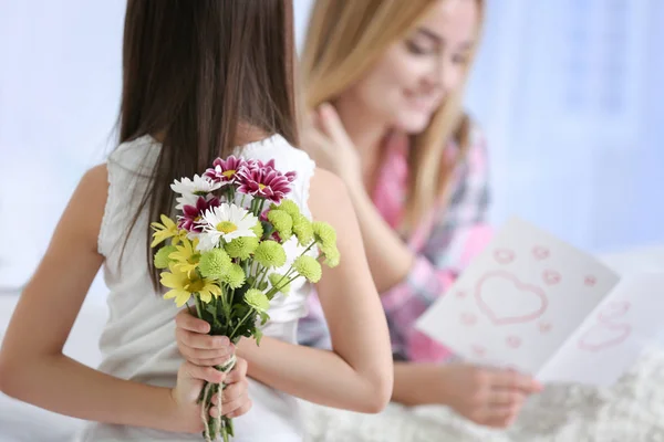 Schattige kleine meisje verbergen bloemen voor haar moeder achter de rug, close-up. Mother's day concept — Stockfoto