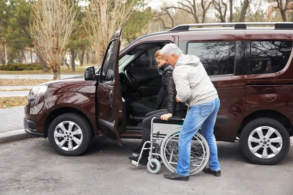 Hombre ayudando a la mujer a sentarse en silla de ruedas — Foto de Stock