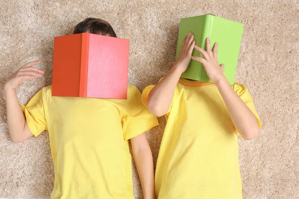 Брати-близнюки з книгами, що лежать на килимі — стокове фото