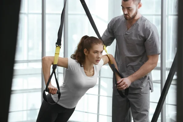 Concepto de rehabilitación. Mujer joven haciendo ejercicios bajo supervisión fisioterapeuta —  Fotos de Stock