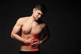 Mladý muž trpící bolesti břicha na černém pozadí. Zdravotní péče koncept