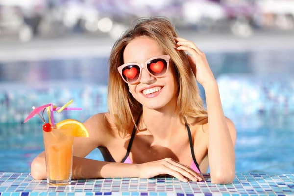 Giovane bella donna che indossa occhiali da sole con cuori in piscina — Foto Stock