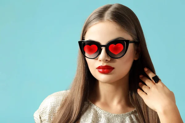 Young beautiful woman wearing sunglasses with hearts on color background — Stock Photo, Image