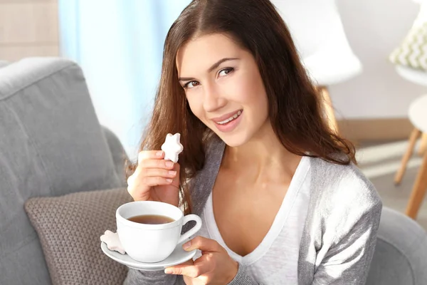 Mujer joven bonita con sabrosa galleta y taza de té en casa — Foto de Stock