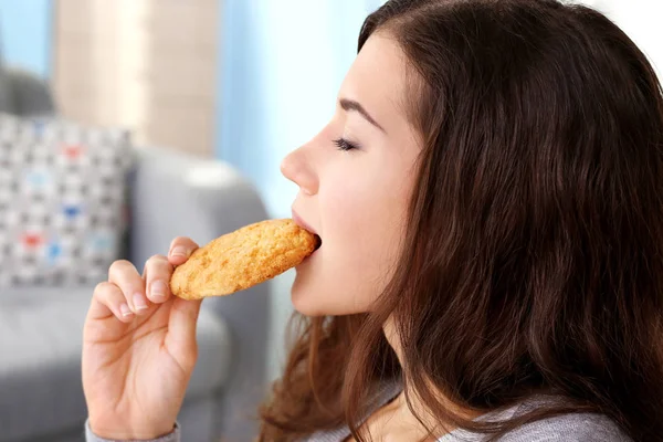 Όμορφη νεαρή γυναίκα τρώει νόστιμο cookie στο σπίτι, κλείστε επάνω — Φωτογραφία Αρχείου