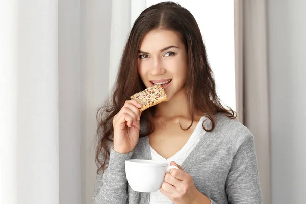 Mujer joven bonita con sabrosa galleta y taza de té en casa — Foto de Stock