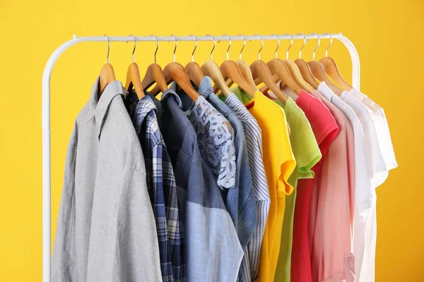 Kleiderbügel mit bunten Kleidern auf gelbem Hintergrund — Stockfoto