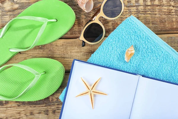 Concepto de vacaciones. Libro abierto, chanclas, gafas de sol y toalla sobre mesa de madera —  Fotos de Stock