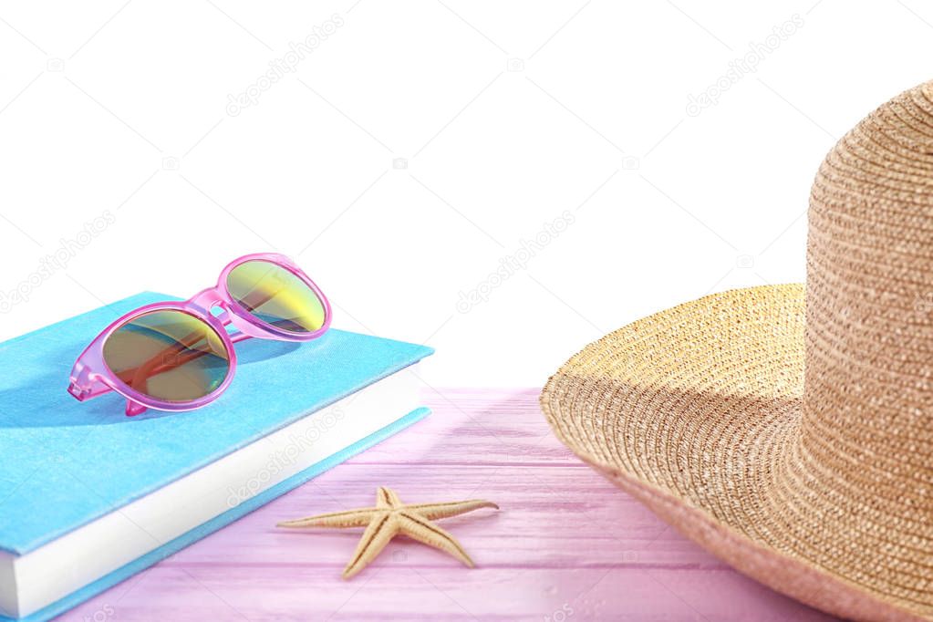 Book, sunglasses and hat on pink wooden table