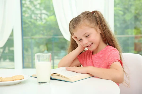 ミルクのガラスのテーブルに座って 本を読んで女の子 — ストック写真