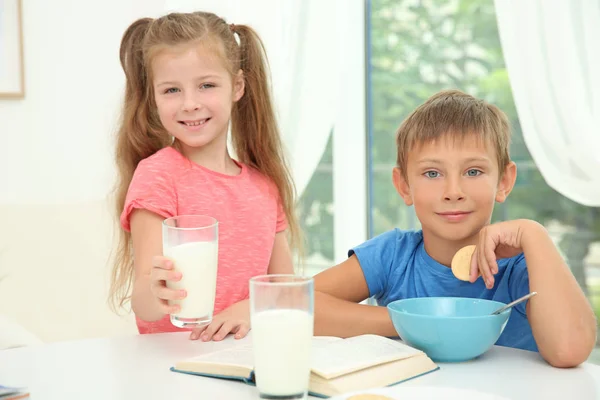 小男孩和女孩坐在桌边与牛奶和书的玻璃 — 图库照片