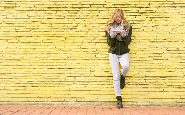 黄色のレンガにスマート フォン立って 若い美しい女性の壁の背景 — ストック写真