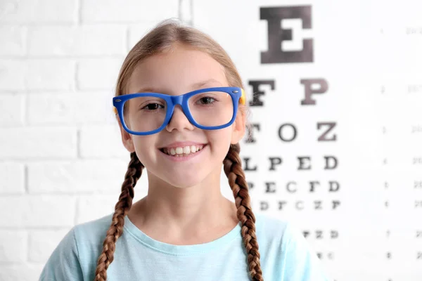 Kleines Mädchen mit Brille auf ophthalmologischem Testdiagramm-Hintergrund — Stockfoto