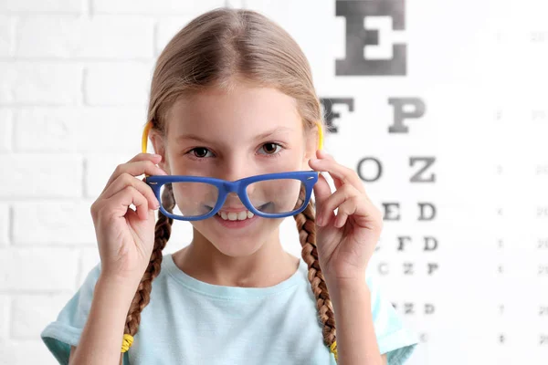 Petite fille avec lunettes sur fond de carte de test ophtalmique — Photo