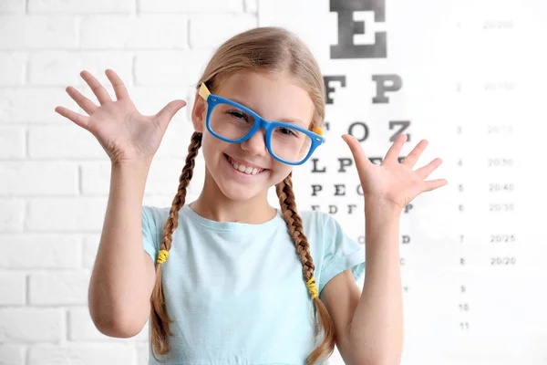 Little girl with spectacles on ophthalmic test chart background — Stock Photo, Image