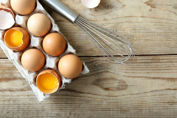 Raw eggs in package with whisk — Stock Photo, Image