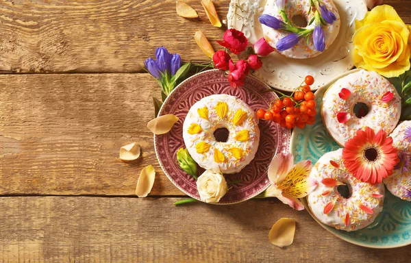 Platen met heerlijke donuts en kleurrijke bloemen — Stockfoto