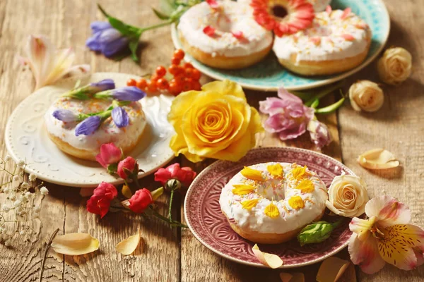 Piatti con deliziose ciambelle e fiori colorati — Foto Stock