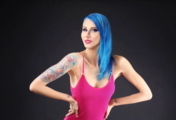 Mooie jonge vrouw met stijlvolle kleur haar en tattoo op donkere achtergrond — Stockfoto