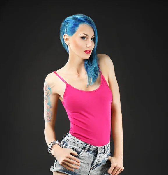 Piękna młoda kobieta z stylowy kolor włosów i tatuaż na ciemnym tle — Zdjęcie stockowe