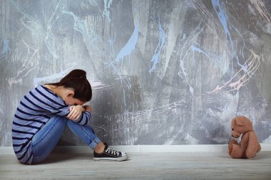 Renk duvar arka plan üzerinde oyuncak ayı ile oturan küçük kız