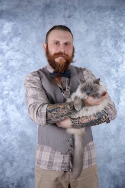 Açık renkli pofuduk kedi ile ekose şapkalı adam genç sakallı