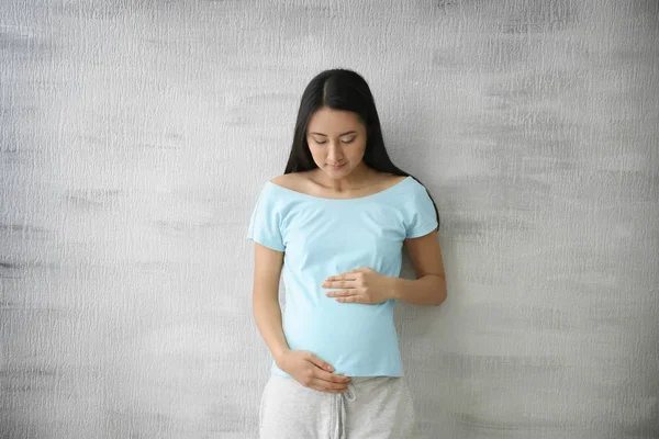 Pregnant Asian woman standing near light wall — Stock Photo, Image