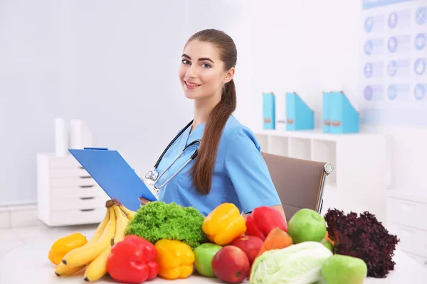 Junge Ernährungsberaterin mit Gemüse und Obst in ihrem Büro — Stockfoto