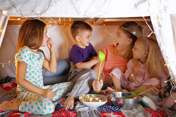 Young woman and cute children playing in hovel at home